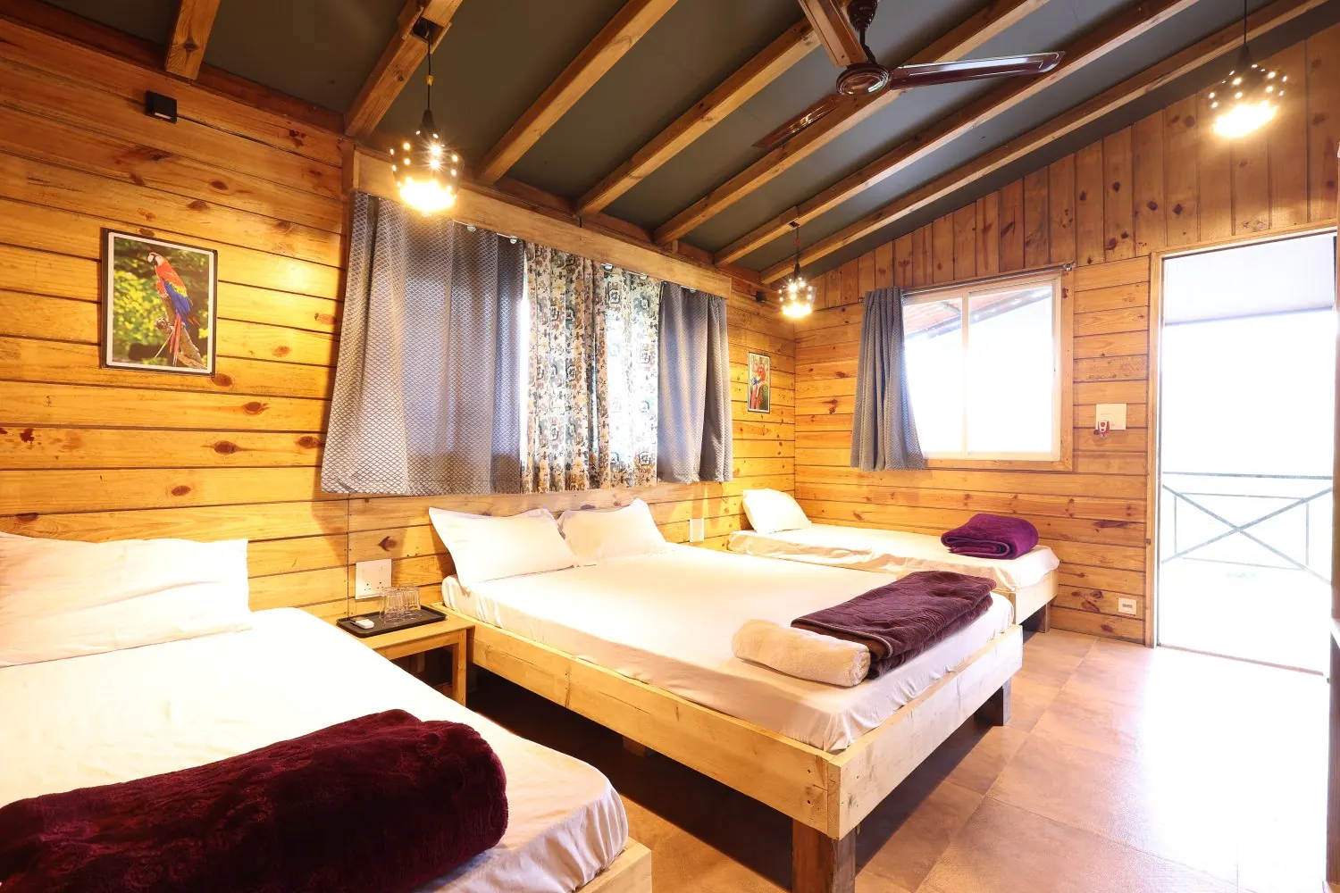 Inside a chalet: queen bed in the middle, a single bed on each side, wooden walls and a ceiling fan